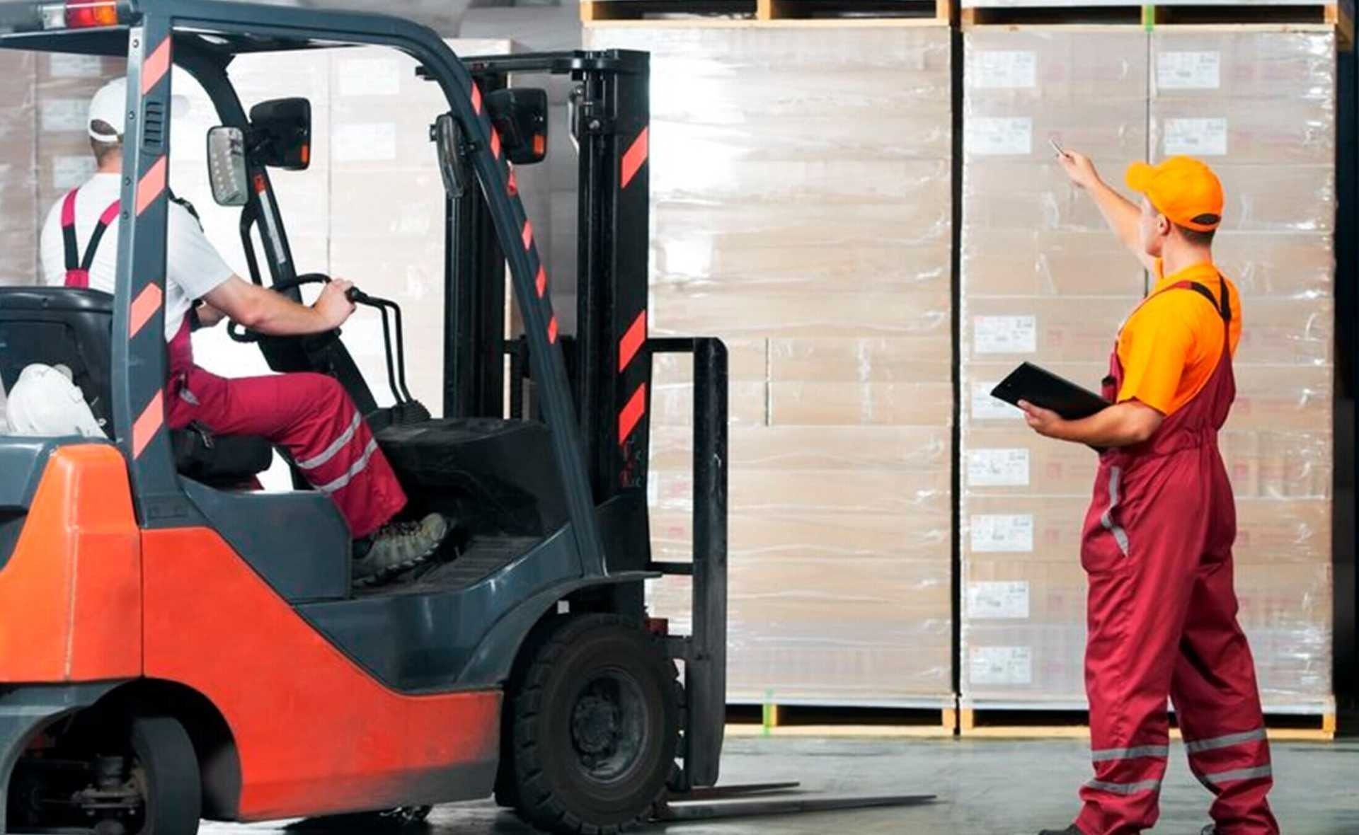 Un hombre está de pie junto a una carretilla elevadora en un almacén.