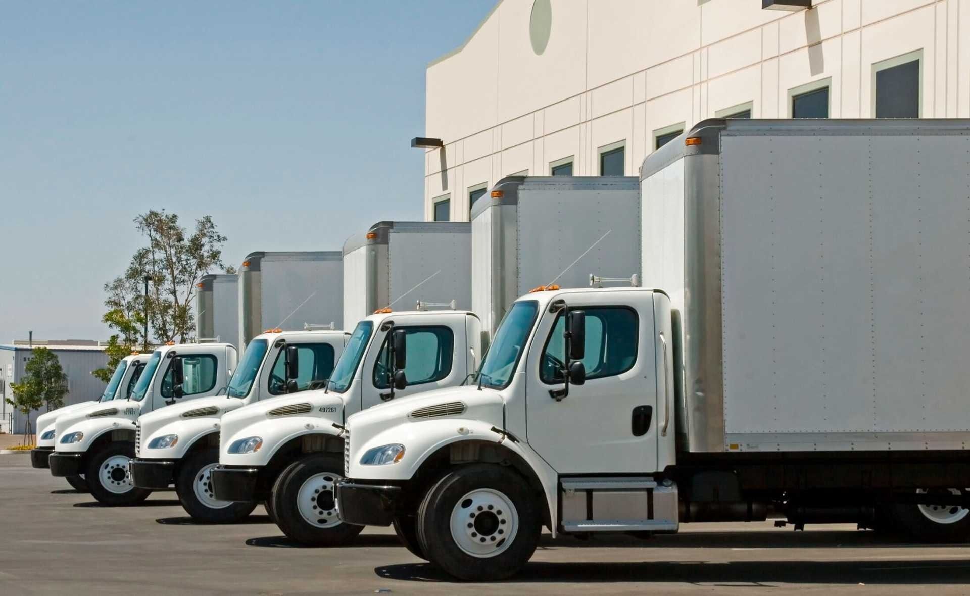 Una fila de camiones blancos están estacionados frente a un edificio