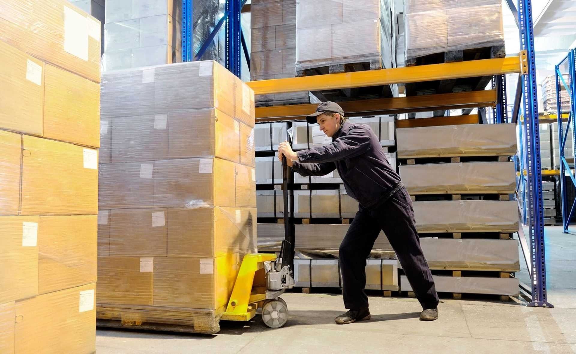 Un hombre empuja una transpaleta en un almacén lleno de cajas.
