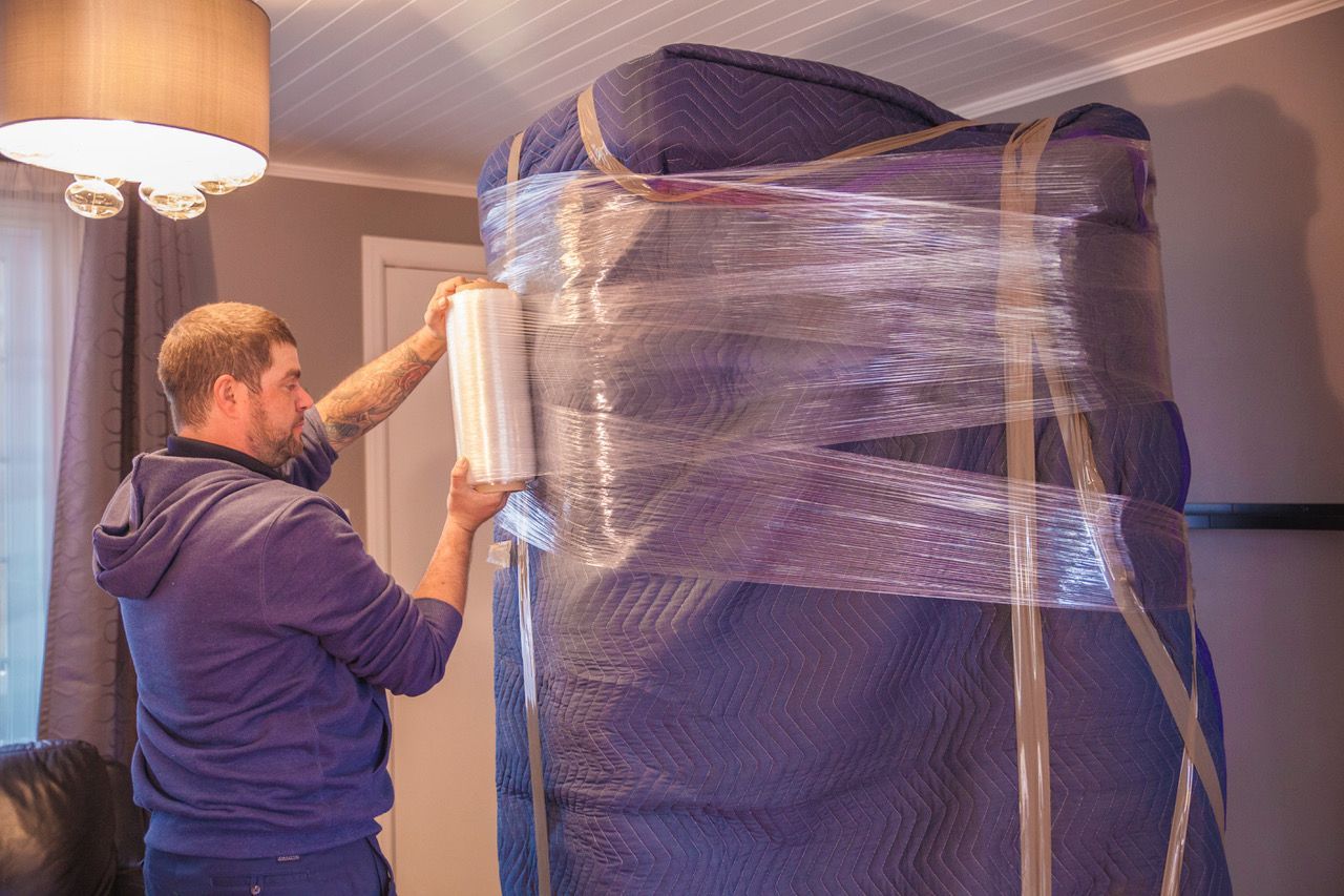 A man is wrapping a large piece of furniture in plastic wrap.