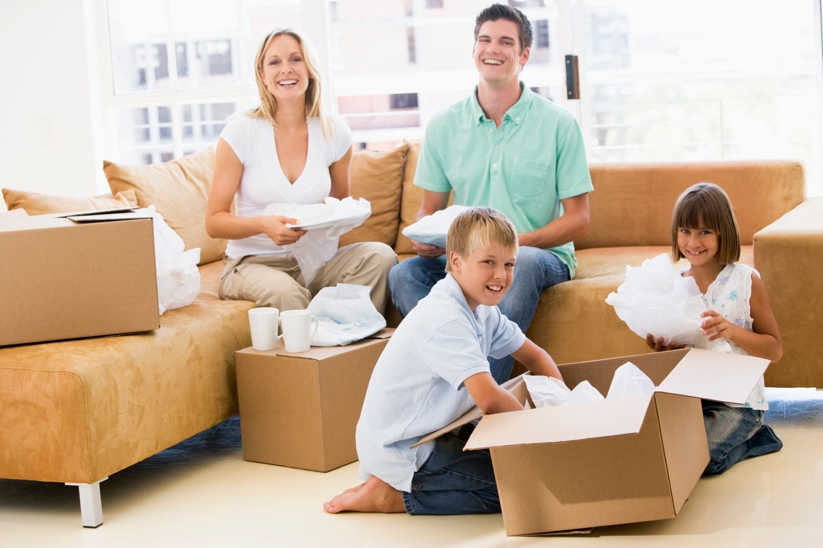 A family is sitting on a couch with cardboard boxes in their living room.