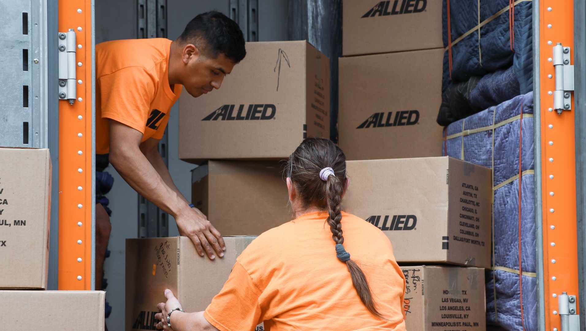 Deux ouvriers en chemises orange chargent des cartons de déménagement Allied dans un camion.
