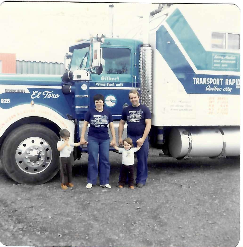 Une famille se tient devant un semi-remorque bleu et blanc, probablement un camion de la société Transport Rapid.