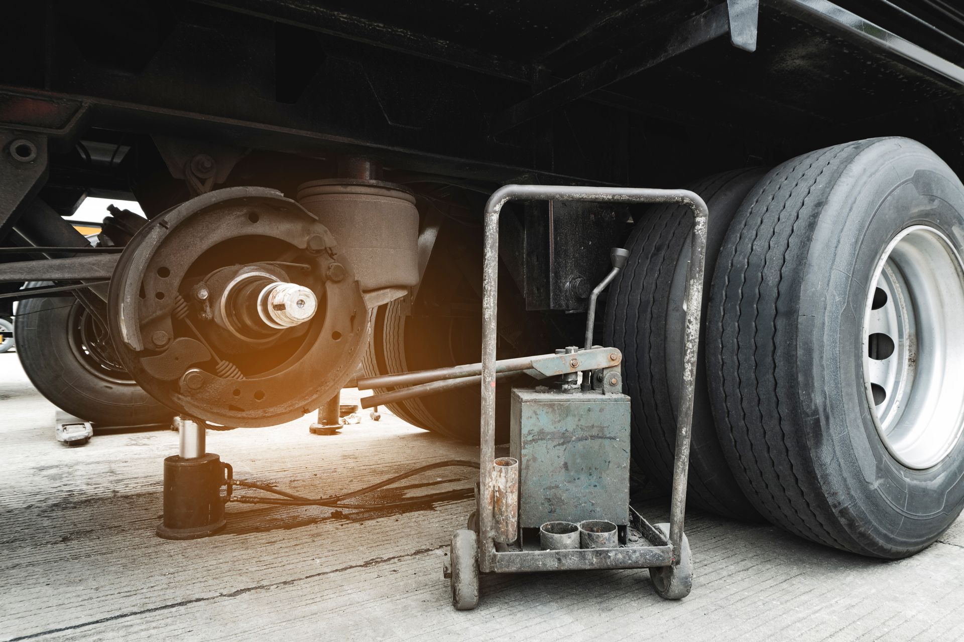 A heavy-duty truck with its wheel removed for brake repair, supported by a jack stand next to a mobile hydraulic tool.