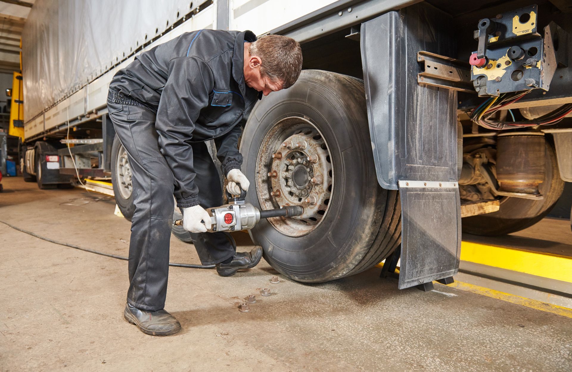 A person wearing a red and black work glove inspects the tread of a large truck tire in a garage.