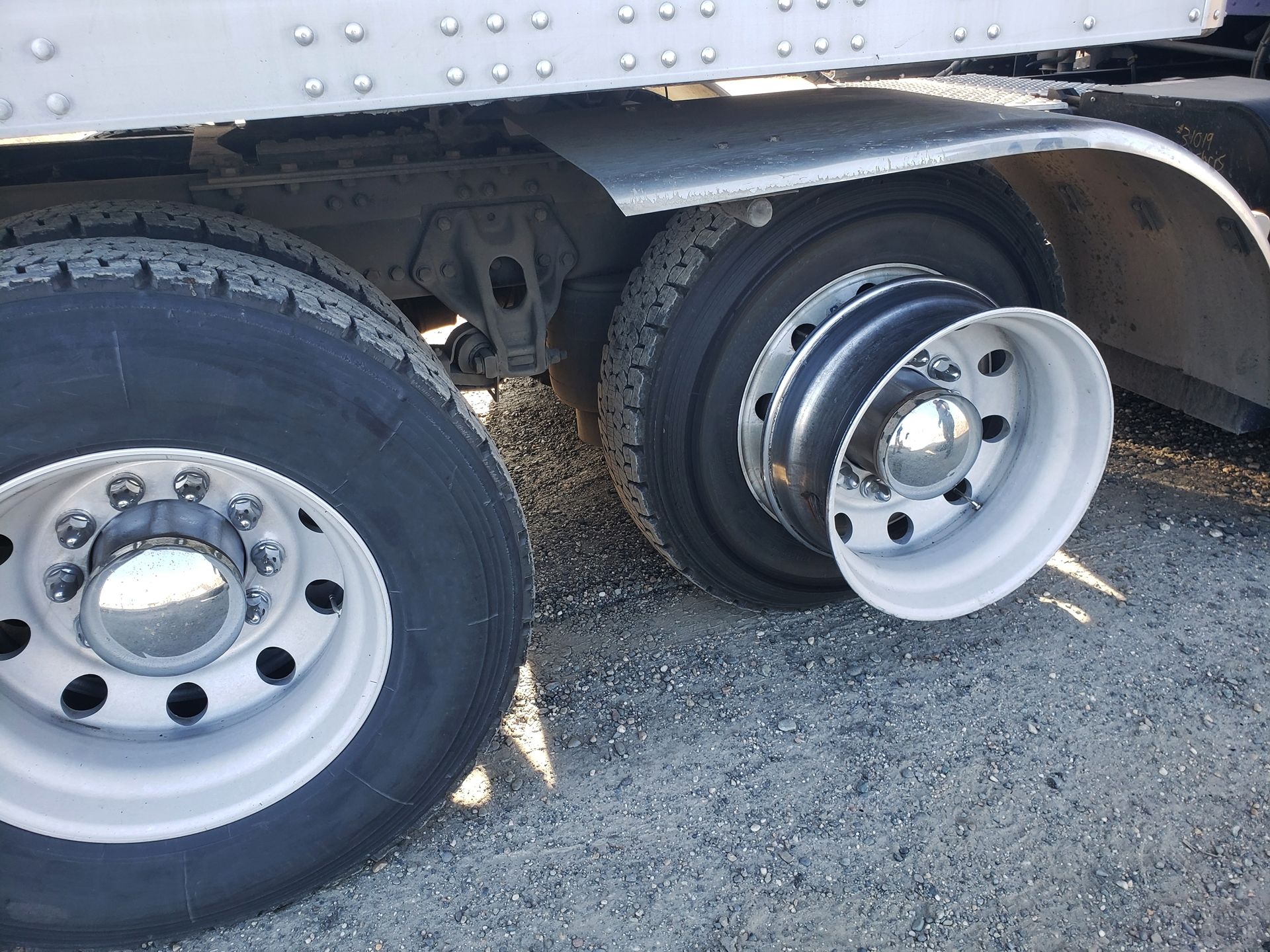 A semi-truck with two rear wheels, one tire is missing, exposing the empty white metal wheel rim.
