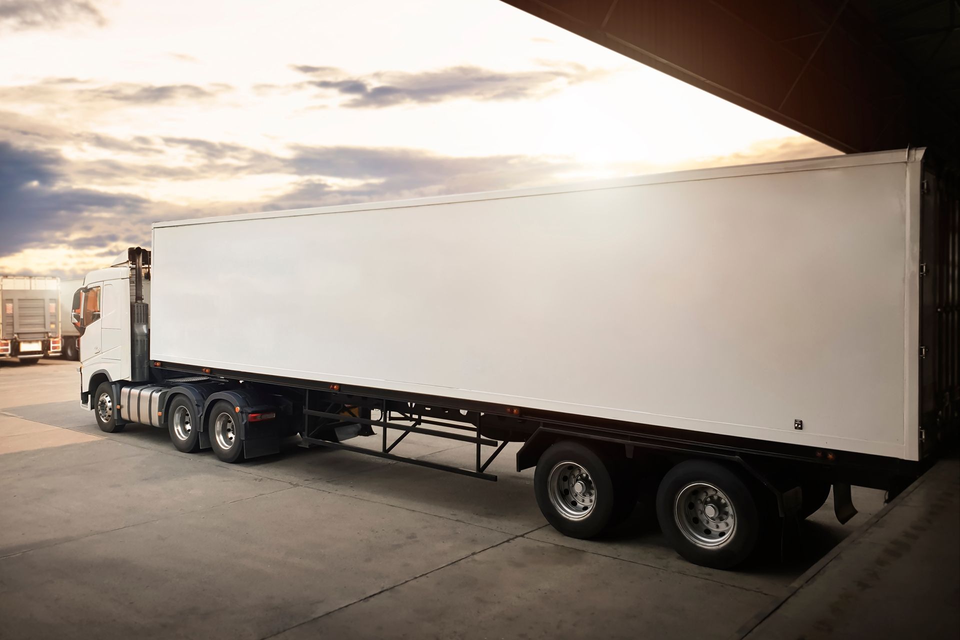 A white semi-truck trailer parked at a loading dock during sunset.