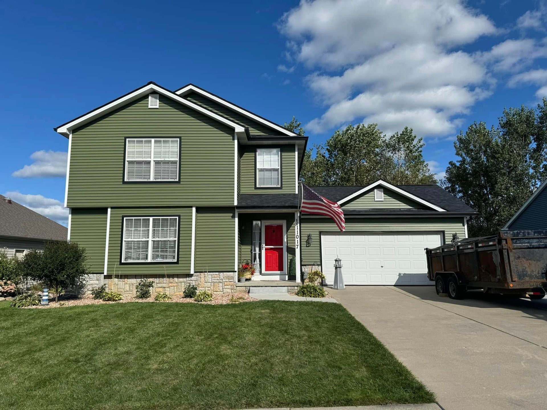 A green house with a red door and an american flag in front of it.