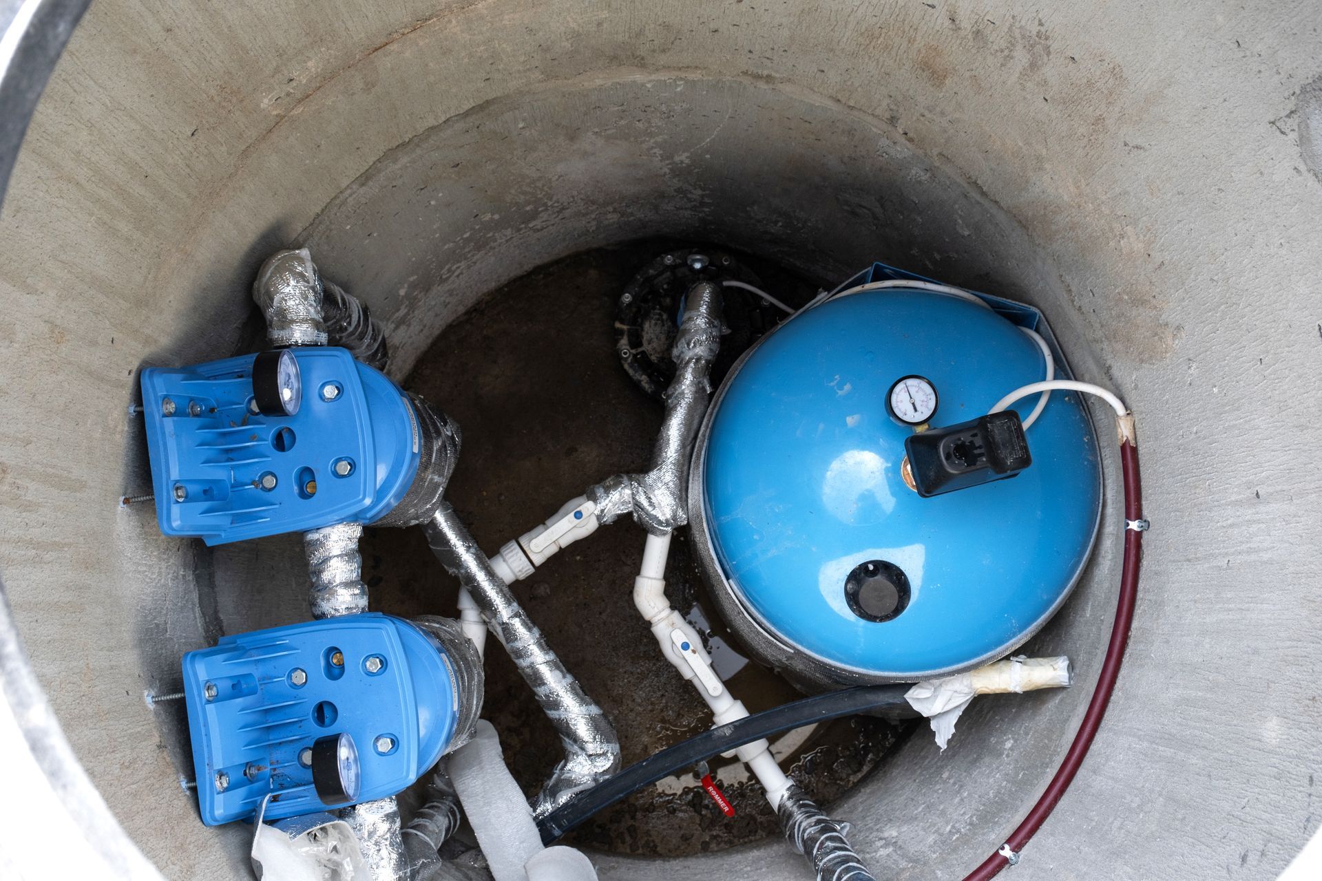 Blue mechanical equipment and hoses inside a concrete utility chamber.