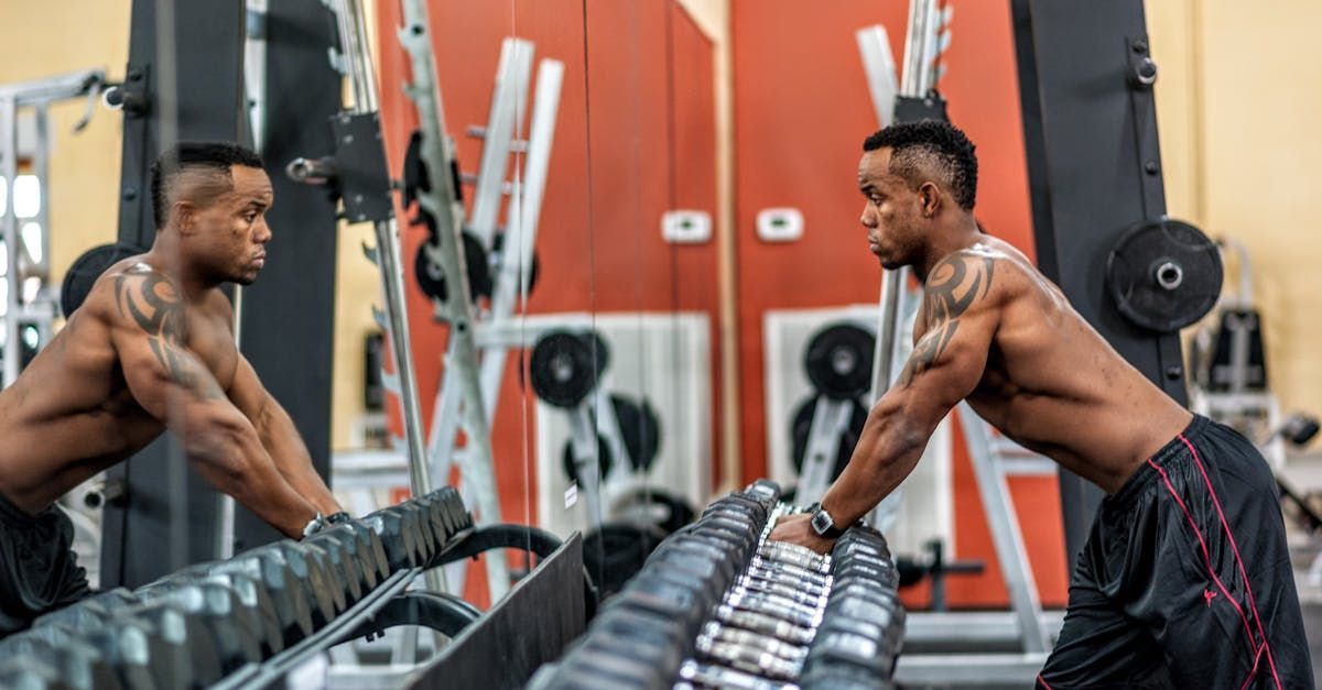 A man is lifting dumbbells in front of a mirror in a gym.