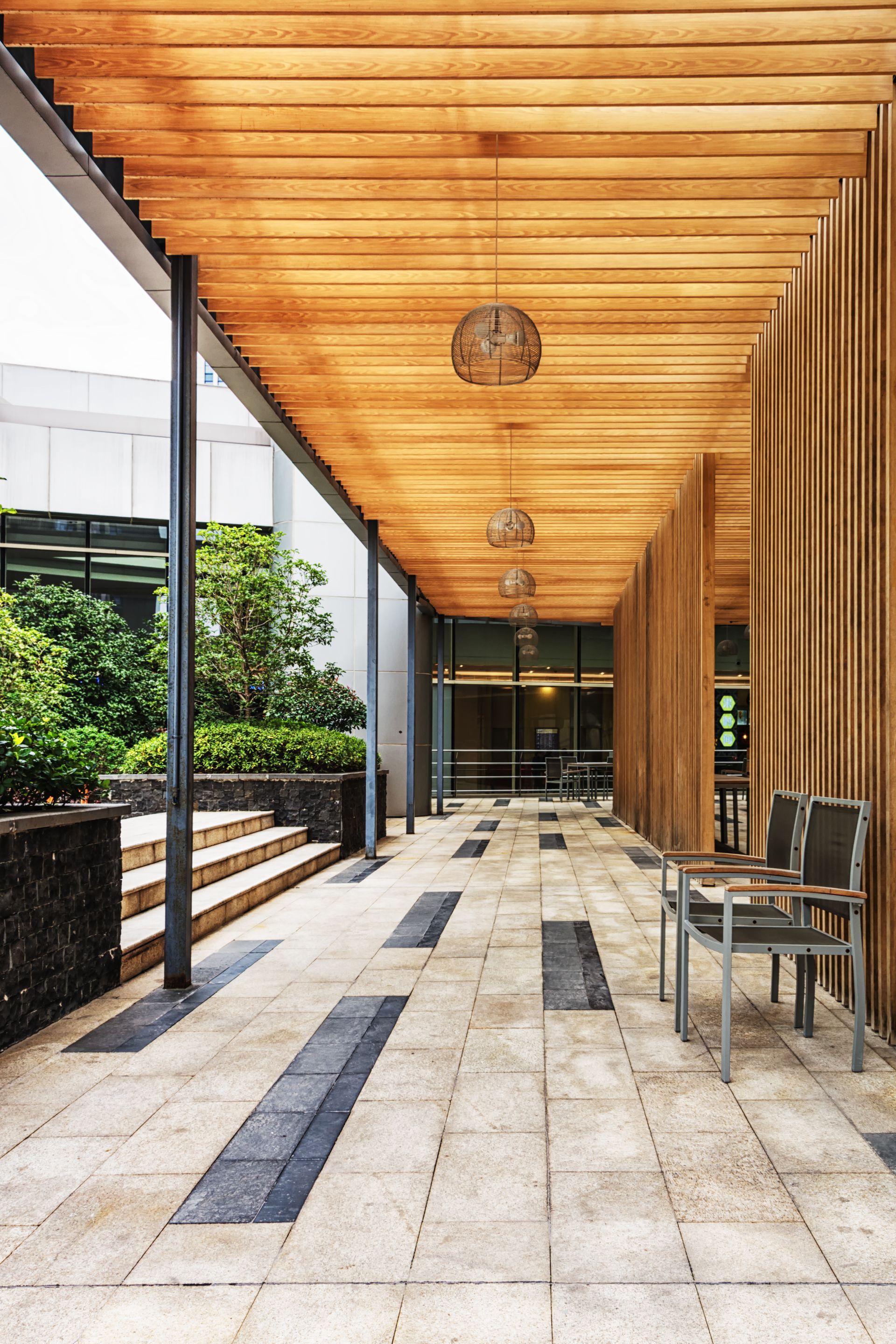 Modern covered outdoor walkway with wood ceiling, stone floor, and a chair at the right side