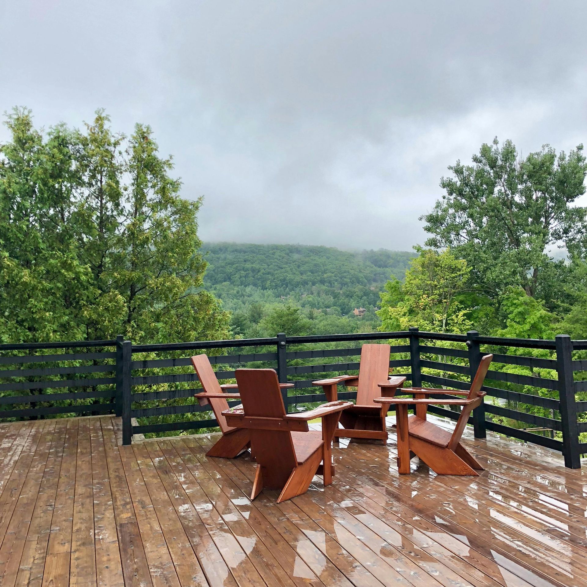 Wooden deck with Adirondack chairs overlooking a misty green forest under cloudy skies