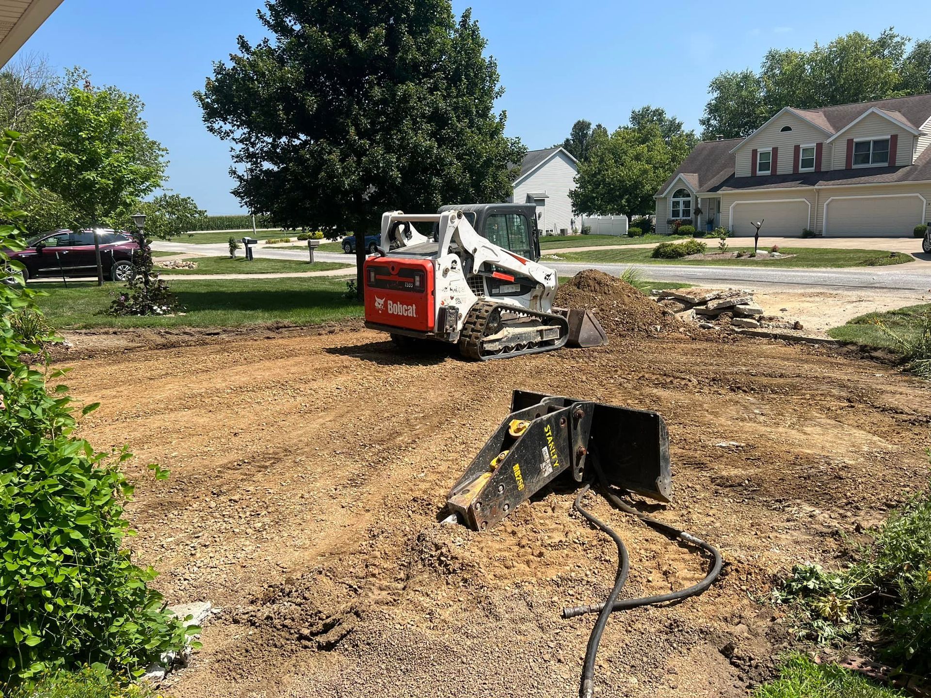 Construction vehicle demolishing concrete in front of an apartment building on a cloudy day.