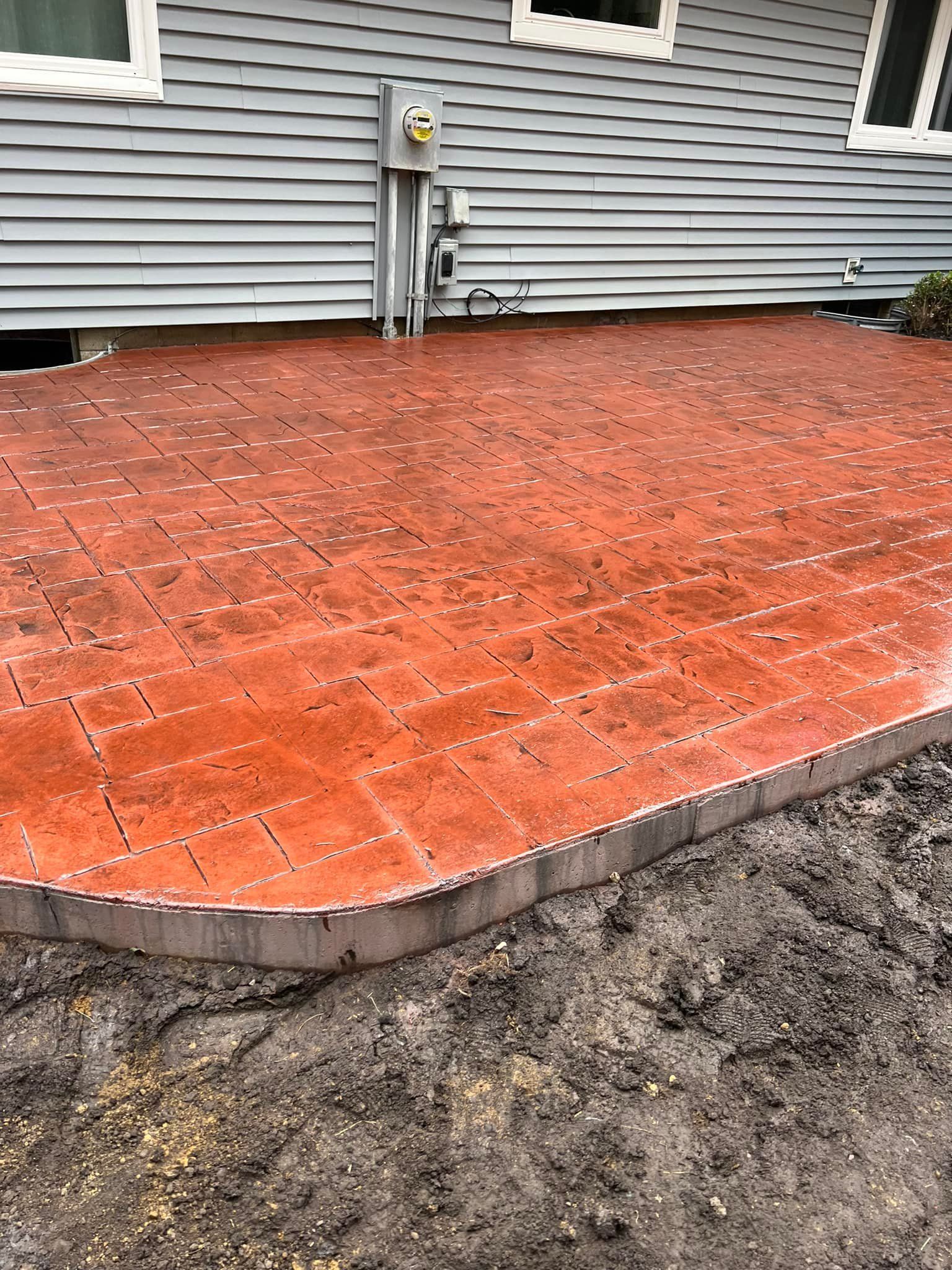 Red brick patio next to a house with gray siding.