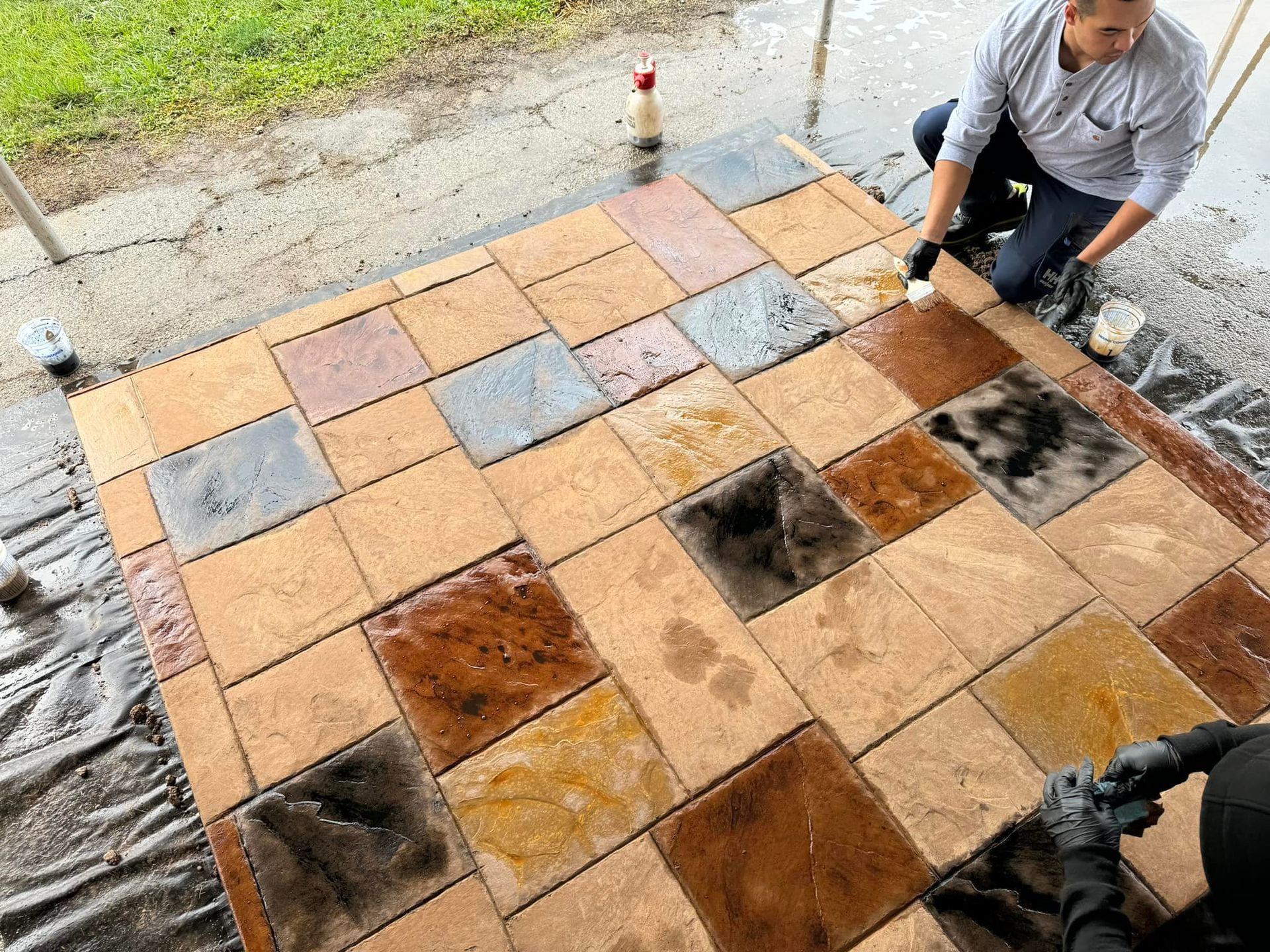 Man applying sealant to a newly laid patio of colorful stone tiles.