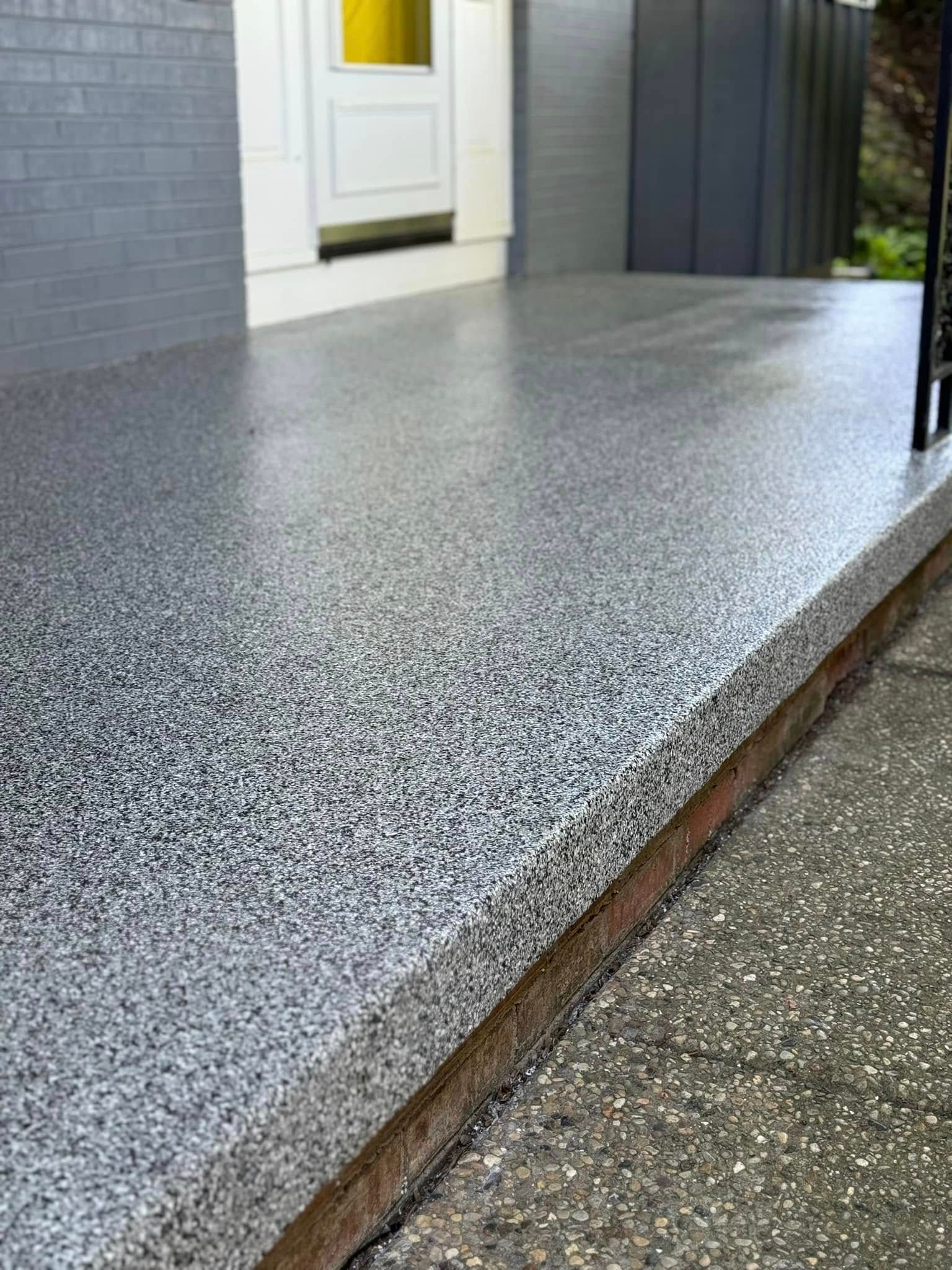 Gray speckled epoxy-coated concrete porch floor, next to a darker concrete sidewalk, leading to a white door.