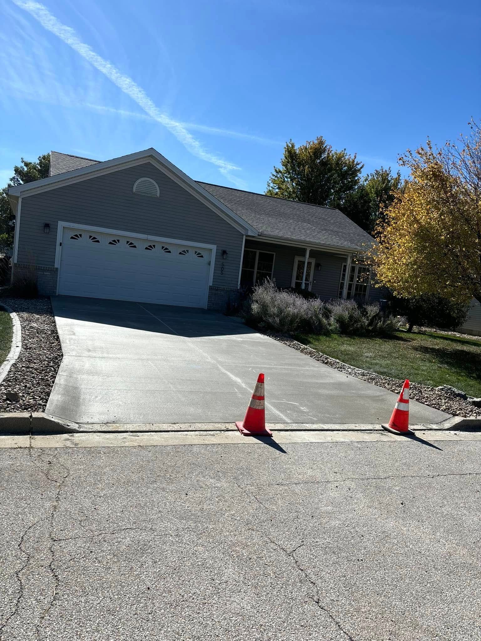 Concrete patio with fire pit, bordered by a low wall, fence, and trees.