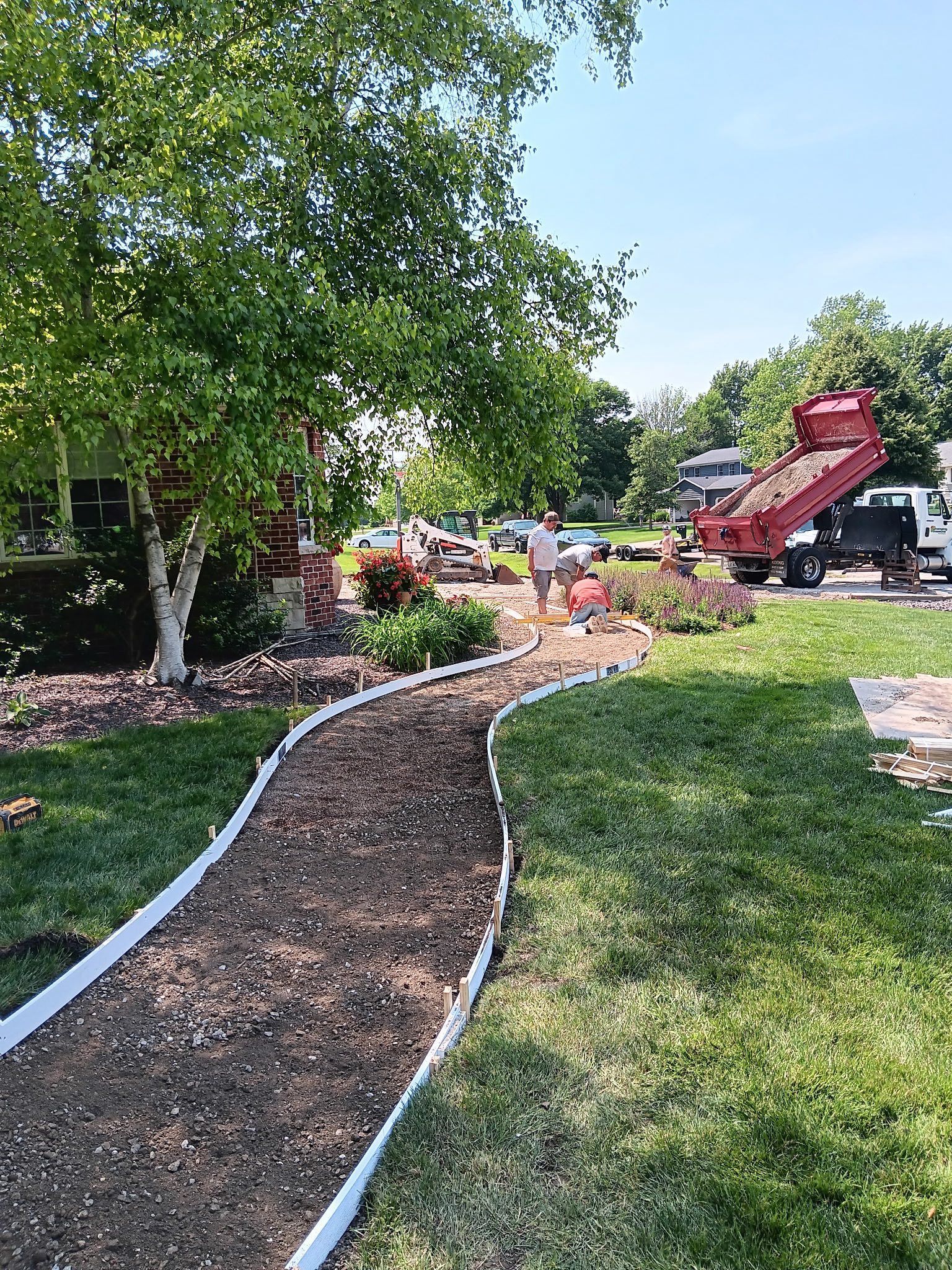 Backyard with a house, patio, and sloped garden overgrown with weeds and plants.
