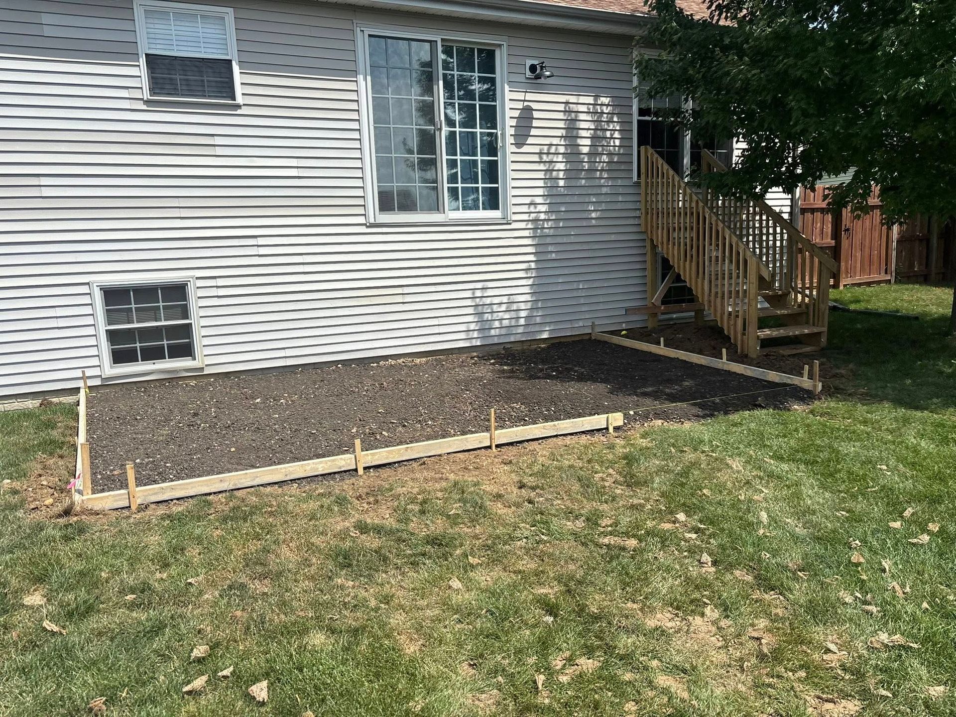 Backyard with a raised wooden flower bed filled with dark soil, beside a house with stairs.