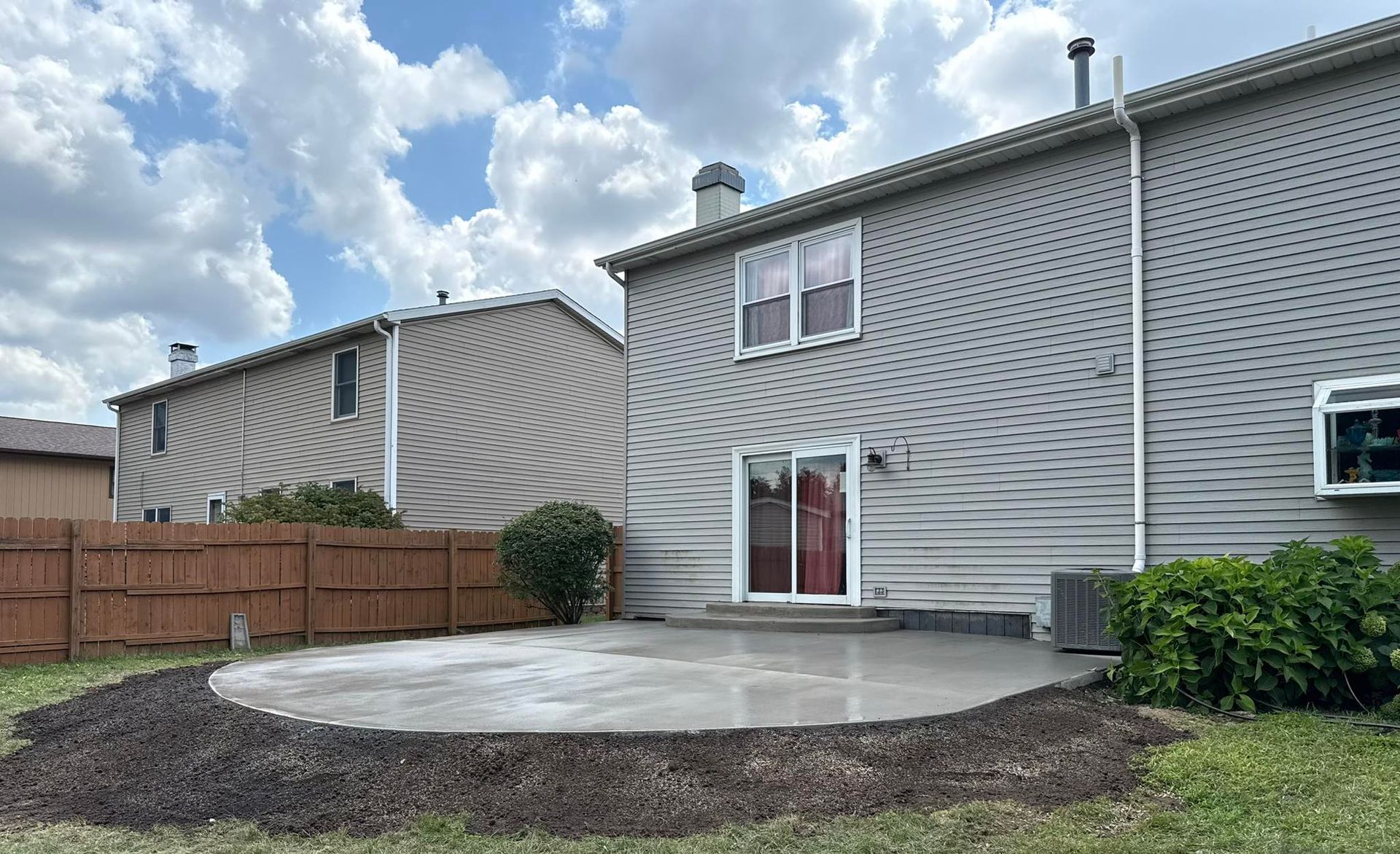 Backyard with a concrete patio, siding house, fence, and cloudy sky.