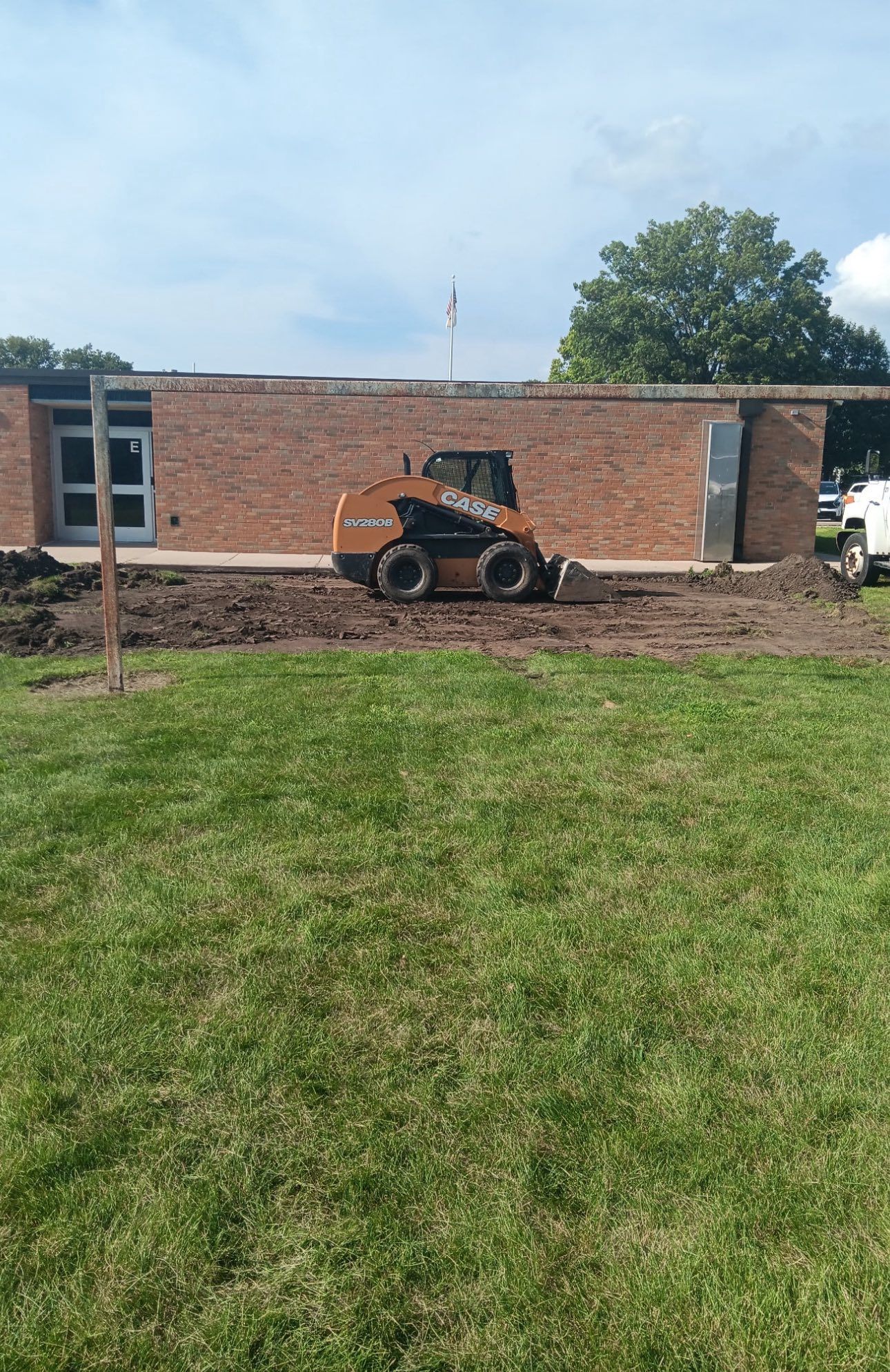 A small orange construction vehicle in front of a brick building on a sunny day.