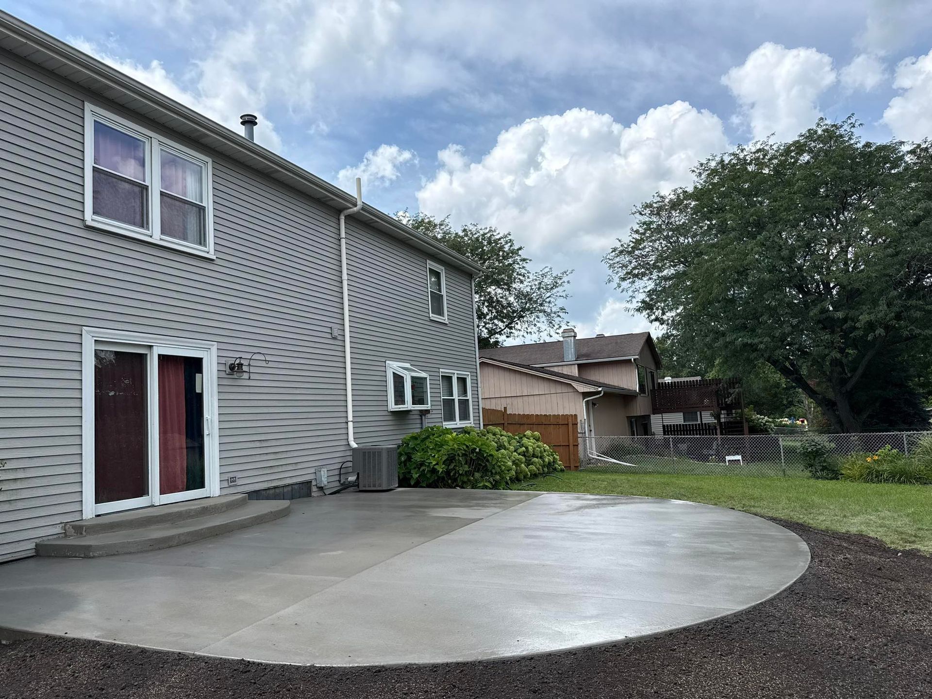Stamped concrete patio with brown coloring next to grass, a white door, and a black fence.