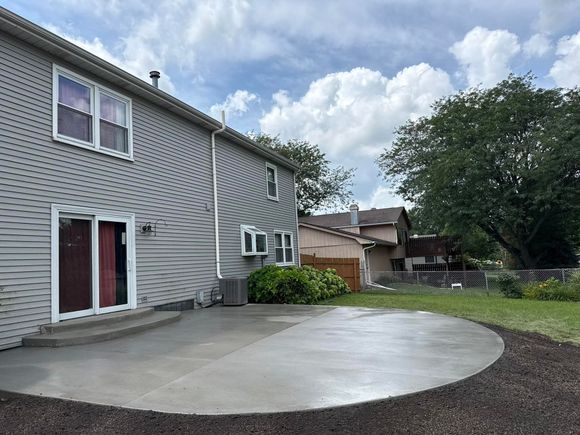 Stamped concrete patio with brown coloring next to grass, a white door, and a black fence.