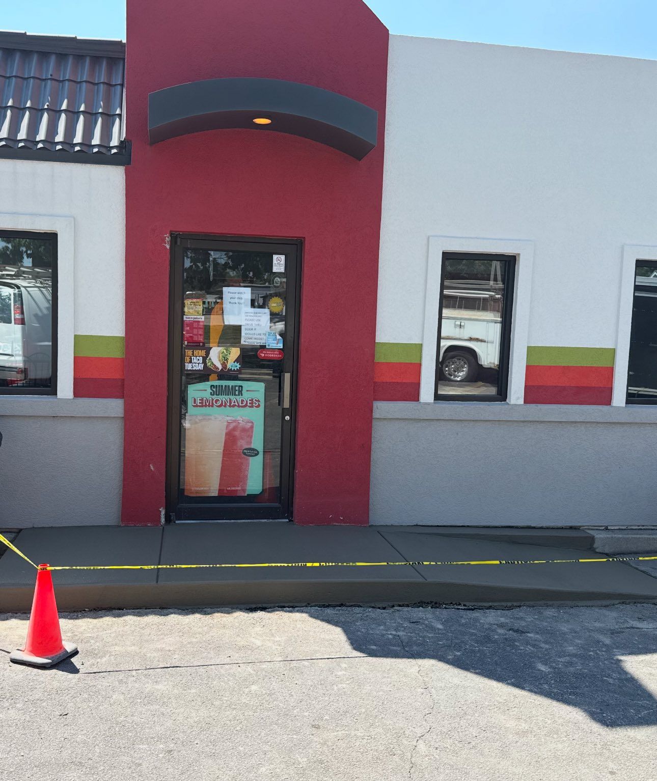 Exterior of a building with a red doorway, caution tape, and a parked vehicle reflecting in a window.
