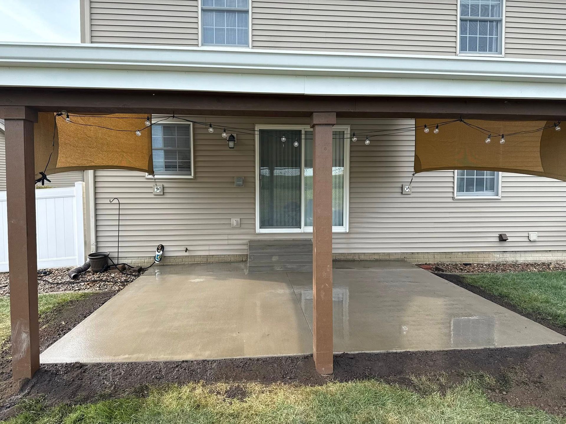 Stamped concrete patio, brown with darker lines, next to grass and white building with door.
