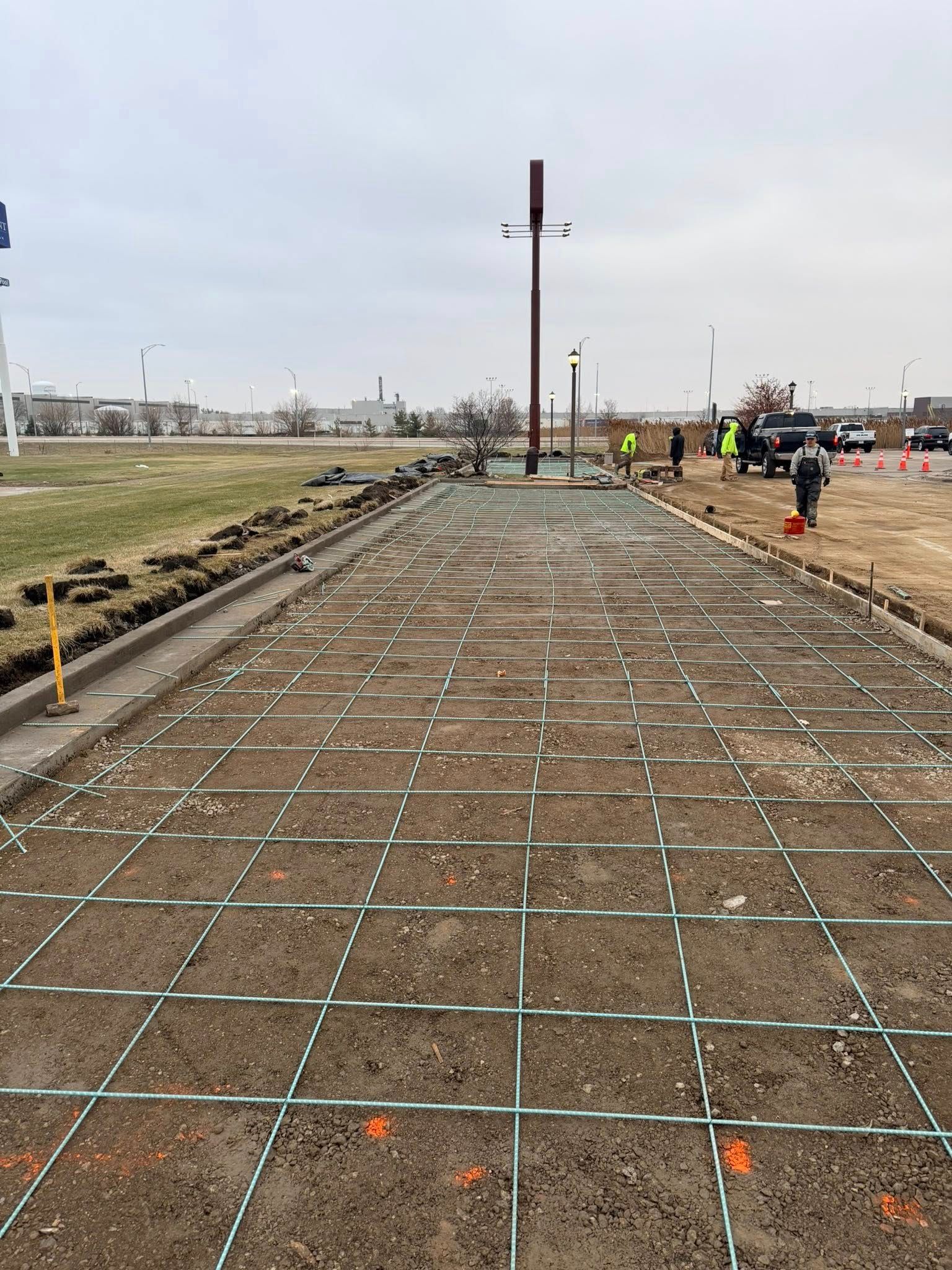 Workers pouring concrete for a driveway in front of a brick house. A wheelbarrow sits nearby.