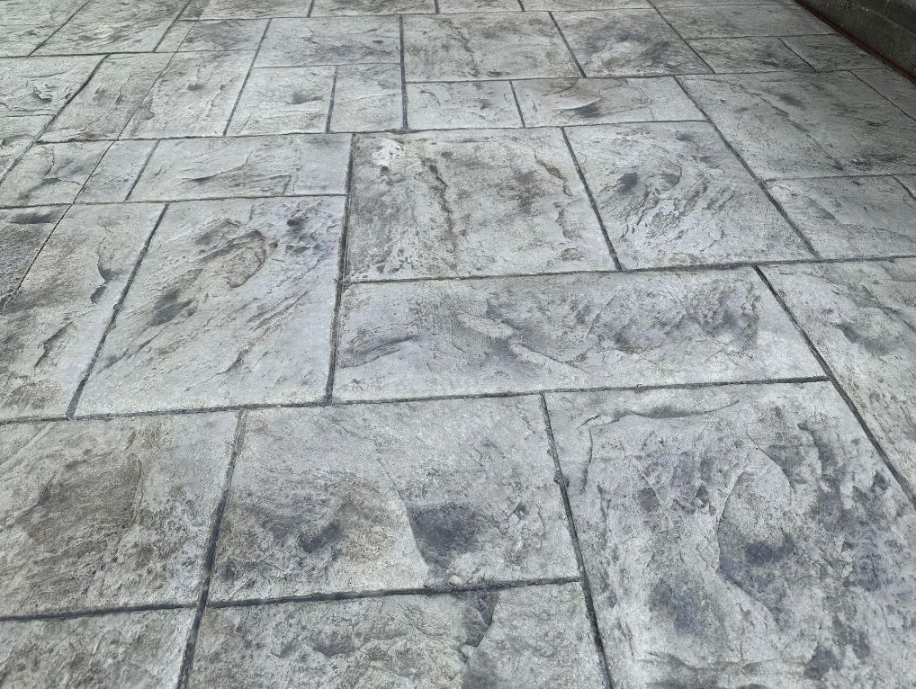 Gray stamped concrete patio with fire pit and outdoor dining set.