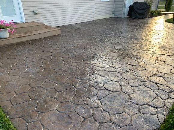 Stamped concrete patio with a fire pit and outdoor dining set on grass.