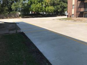 A concrete driveway with a double yellow line, grassy area to the left, and a building on the right.