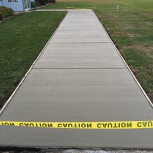 Newly poured concrete sidewalk with caution tape, surrounded by grass.
