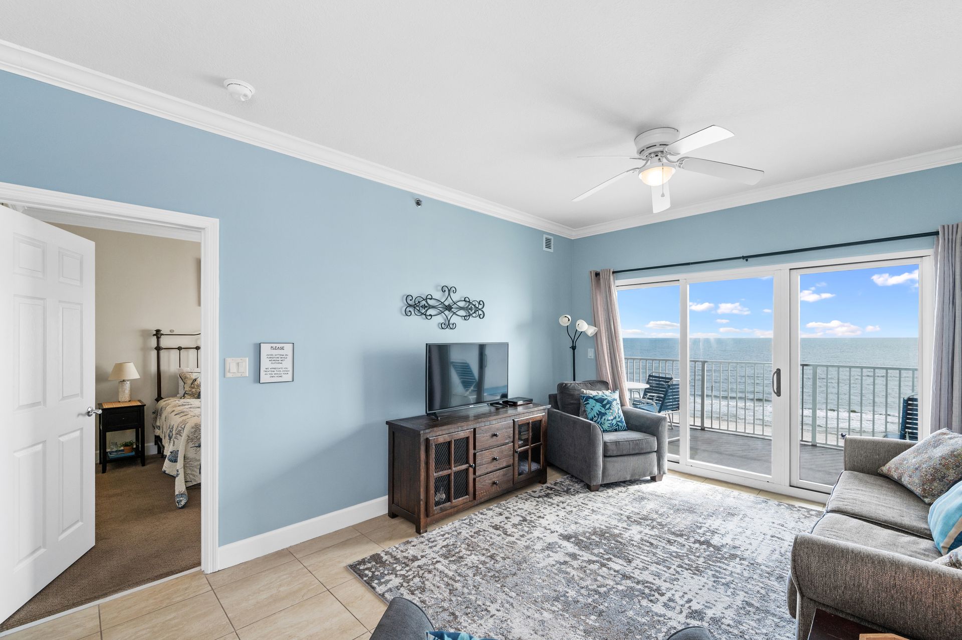Living room with gray furniture, ocean view from balcony, blue walls, and decorative art.