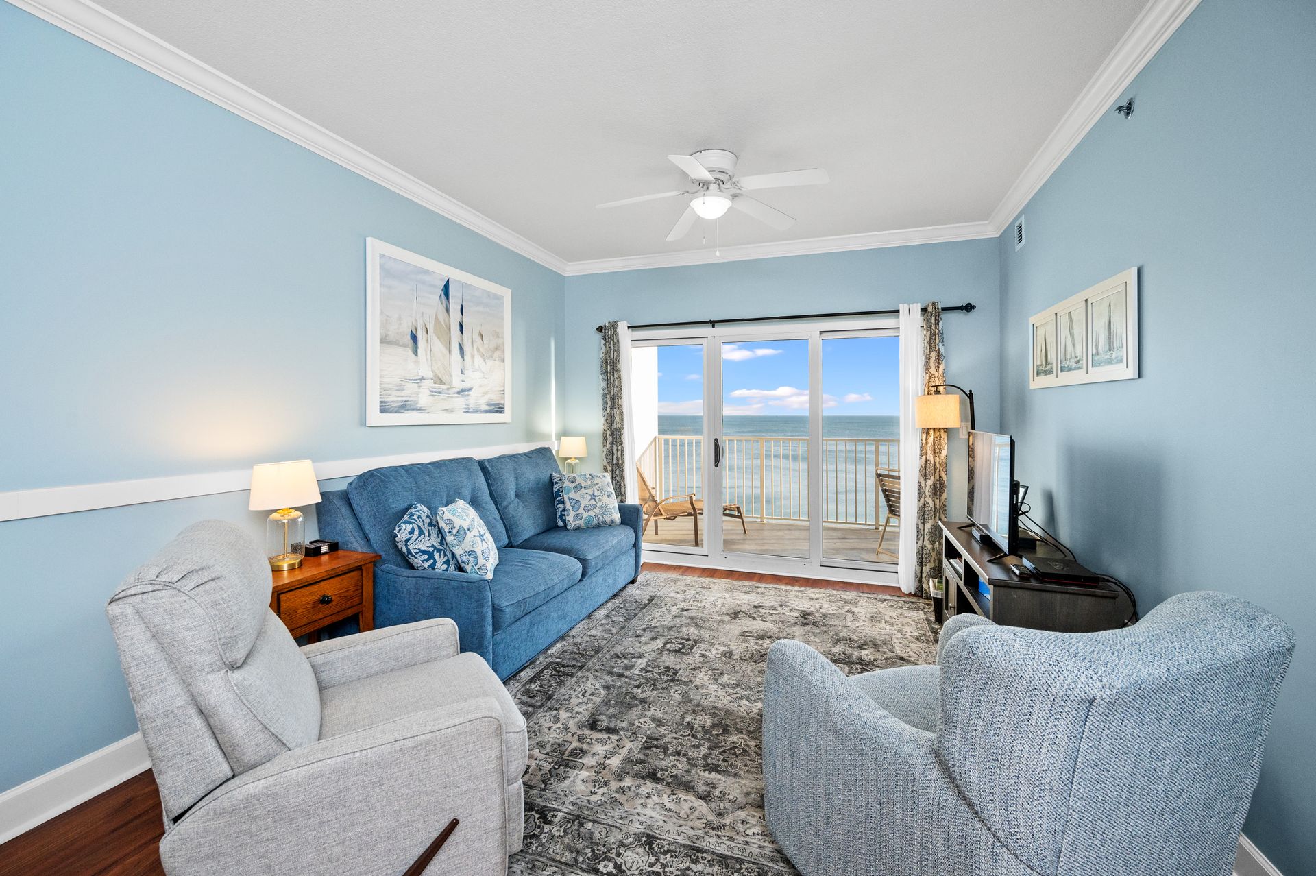 Living room with blue sofa, recliners, ocean view balcony.