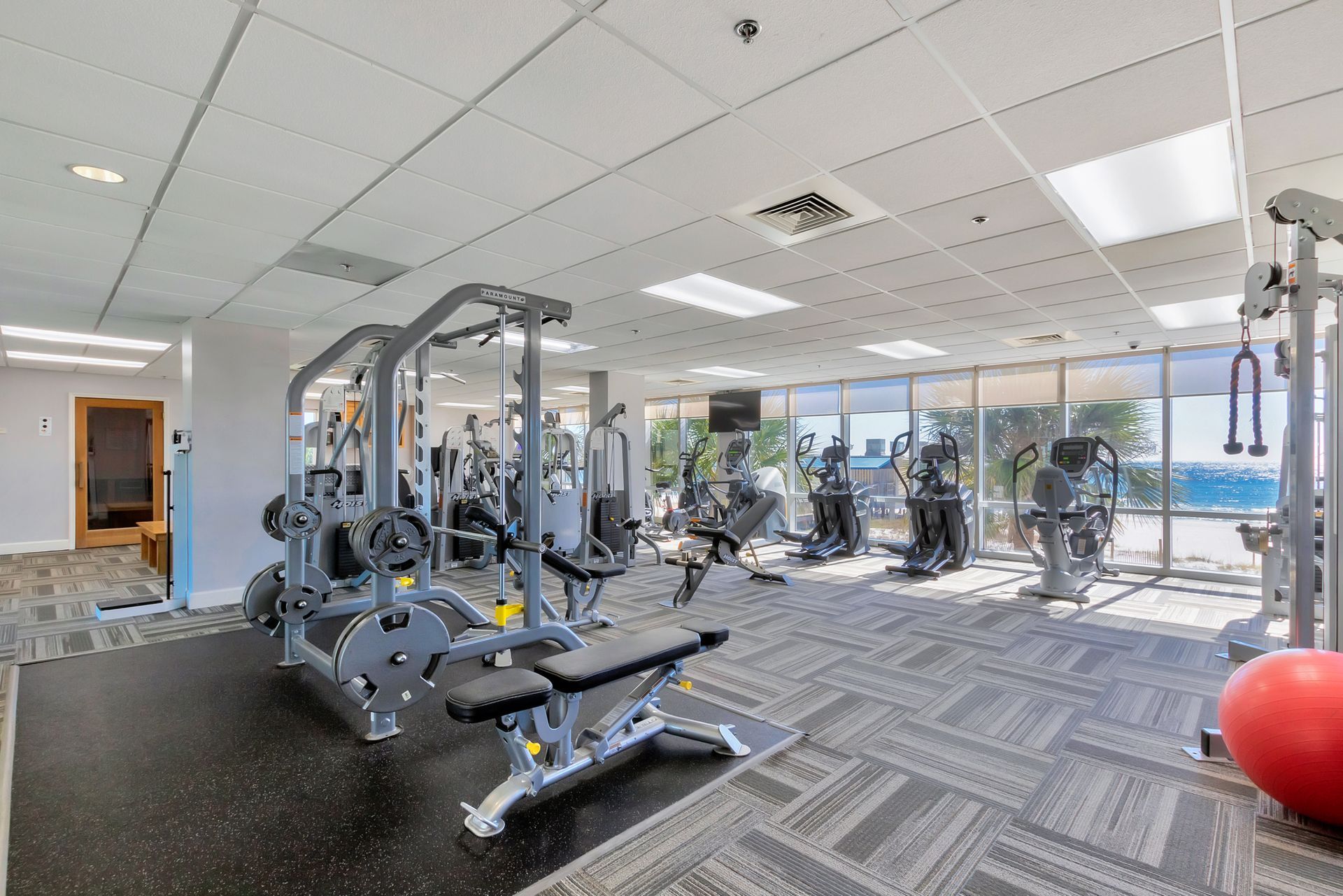 Gym with various exercise machines, floor-to-ceiling windows, and a red exercise ball.