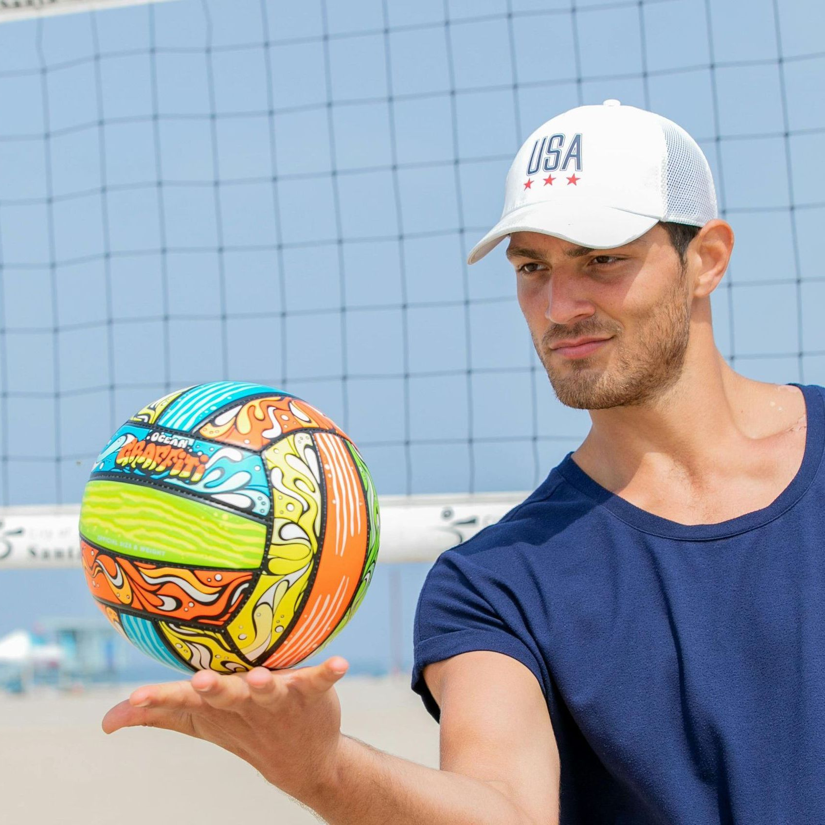 A man wearing a usa hat holds a volleyball in his hand