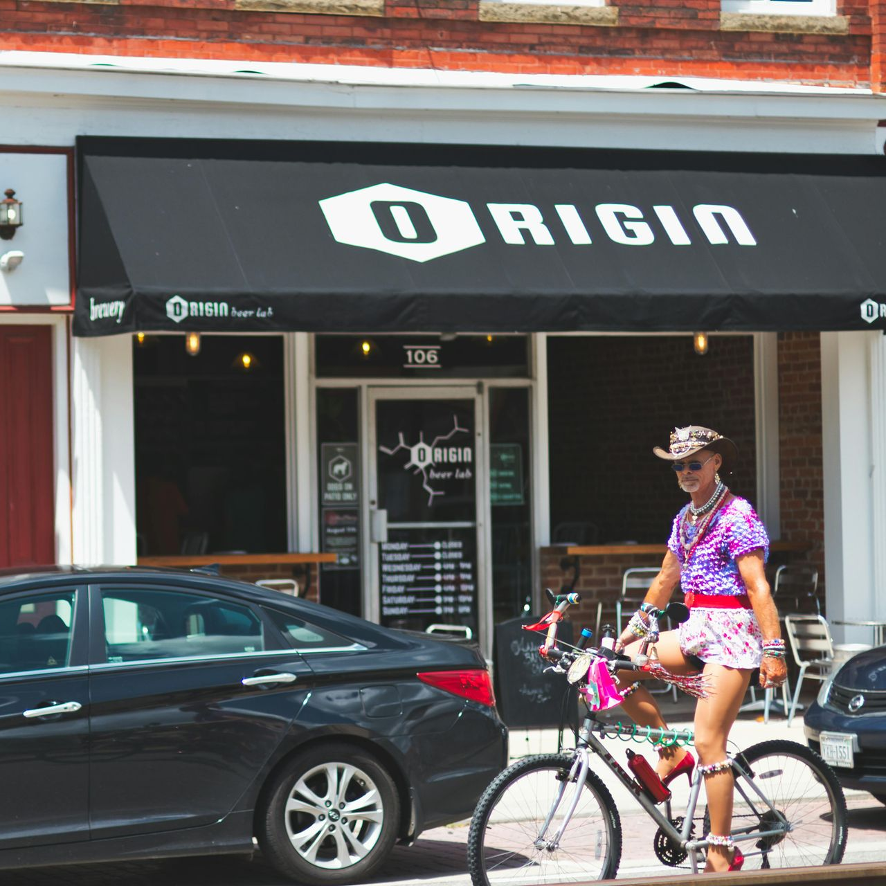 A man is riding a bike in front of a restaurant called origin.