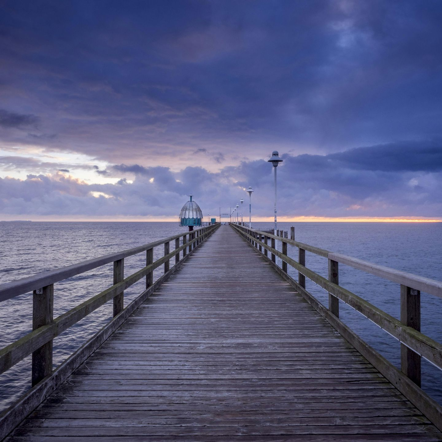 A long wooden pier leading into the ocean at sunset.