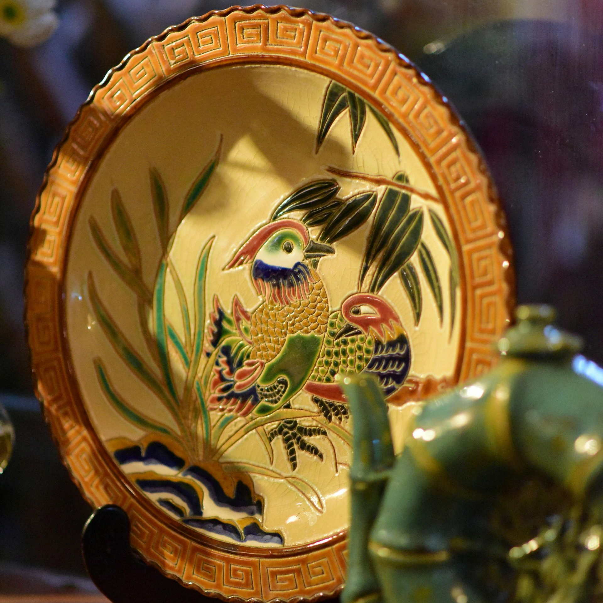 A plate with a bird on it is sitting on a table next to a teapot.