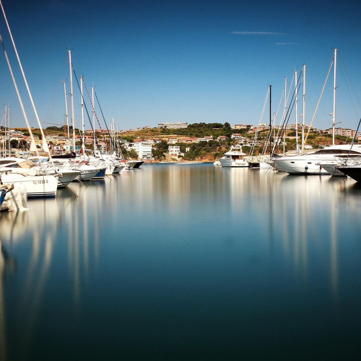 A row of sailboats are docked in a harbor on a sunny day.