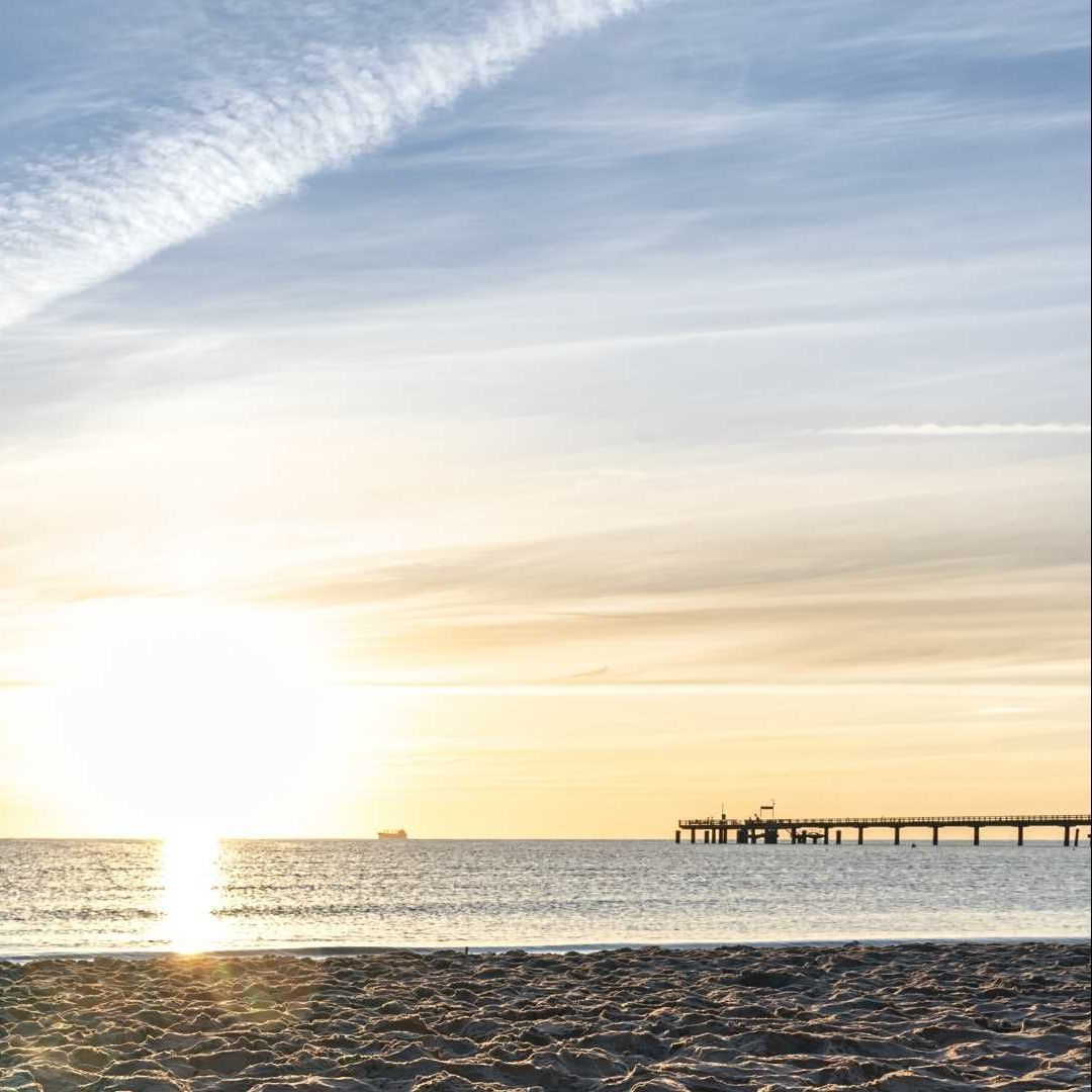 The sun is setting over the ocean with a pier in the distance