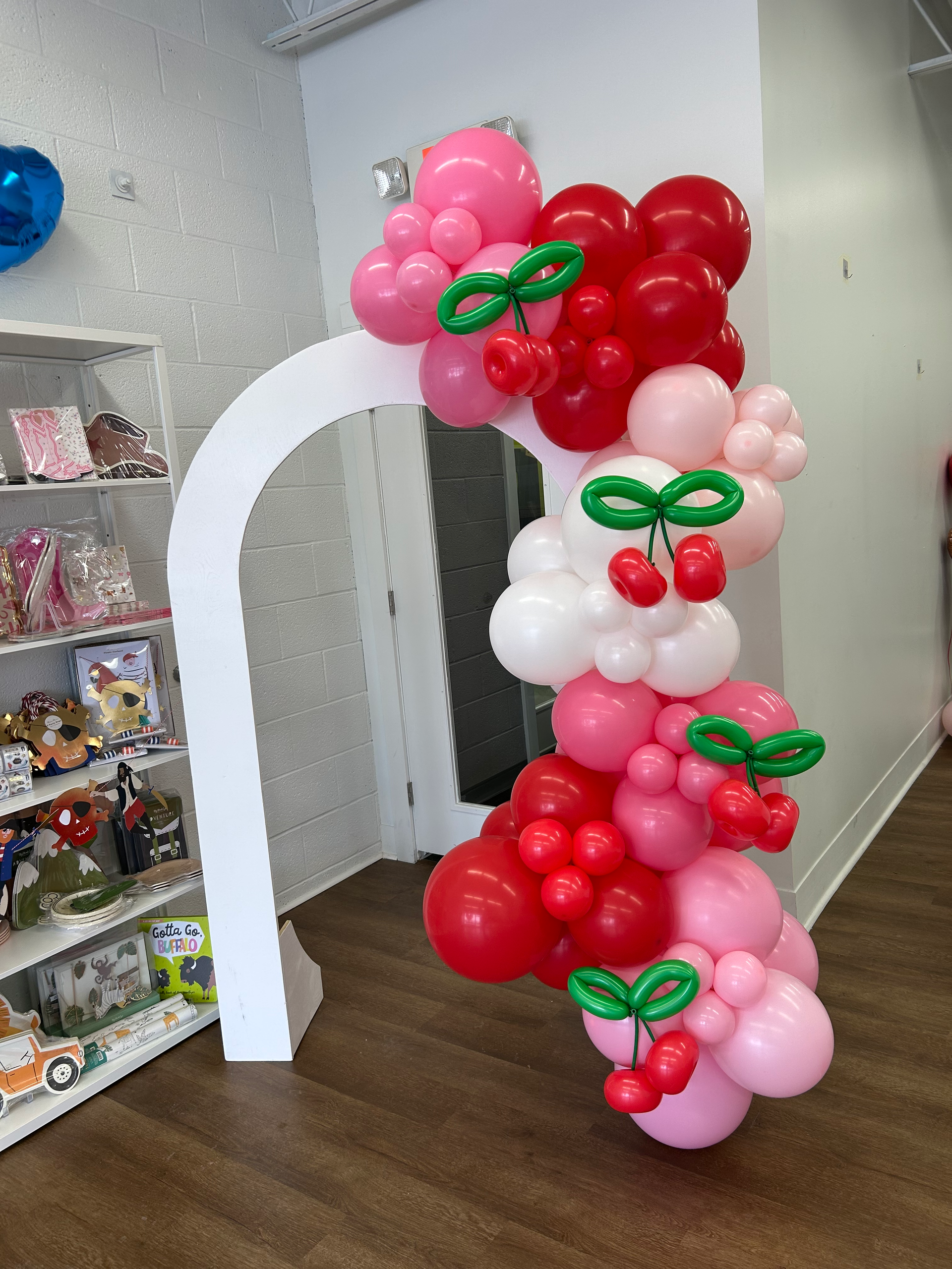 Nicole Boyd with Party Balloon Studio showing an open chiara wall with pink, white,  and red balloon garland with cherries