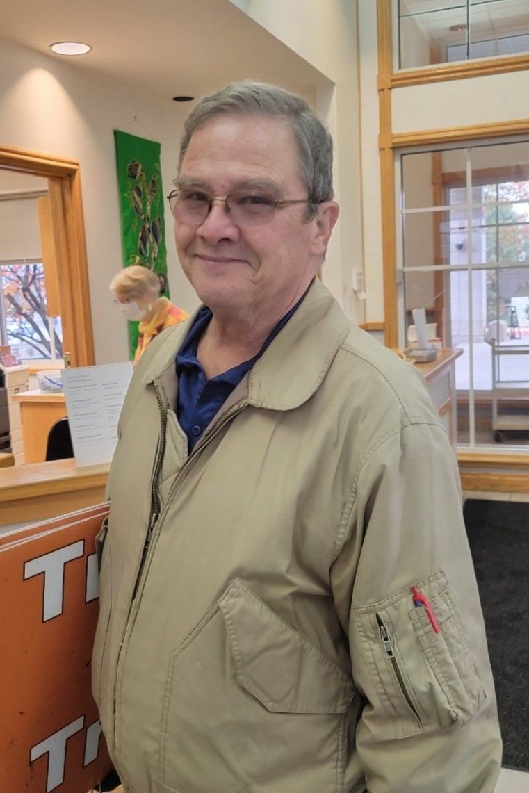 A man wearing a tan jacket and glasses is standing in front of a counter.