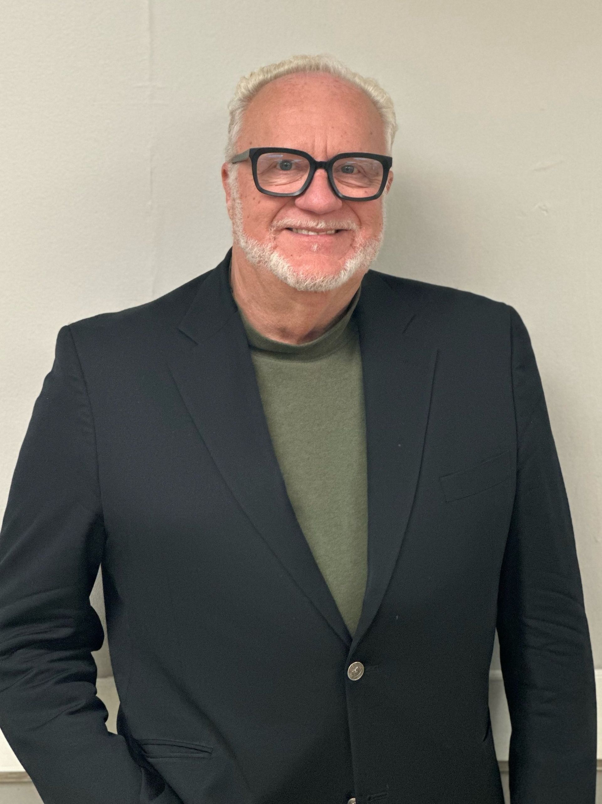 A man in a suit and glasses is standing in front of a white board.