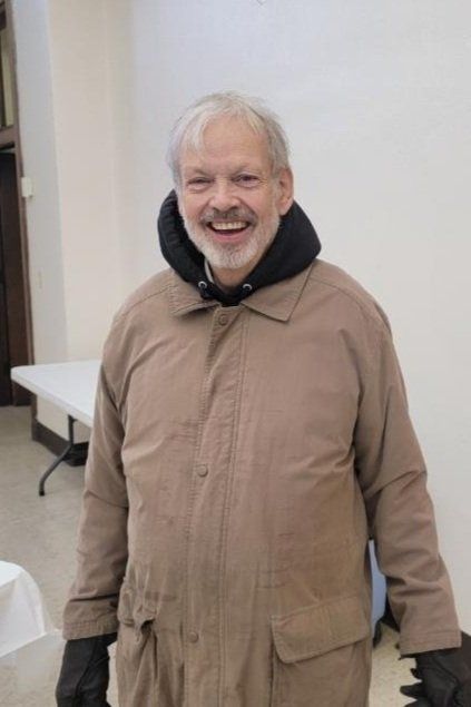 A man wearing a brown jacket and black gloves is smiling for the camera.