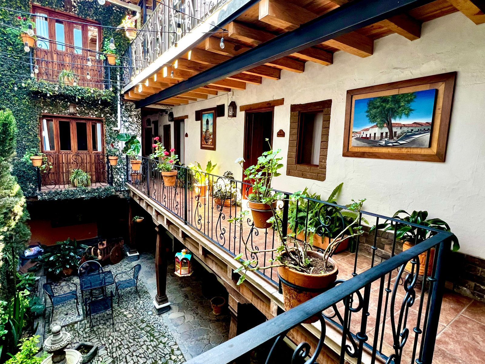 Un balcón con vistas a un patio con arquitectura rústica de madera exuberantes plantas en macetas, barandillas de hierro