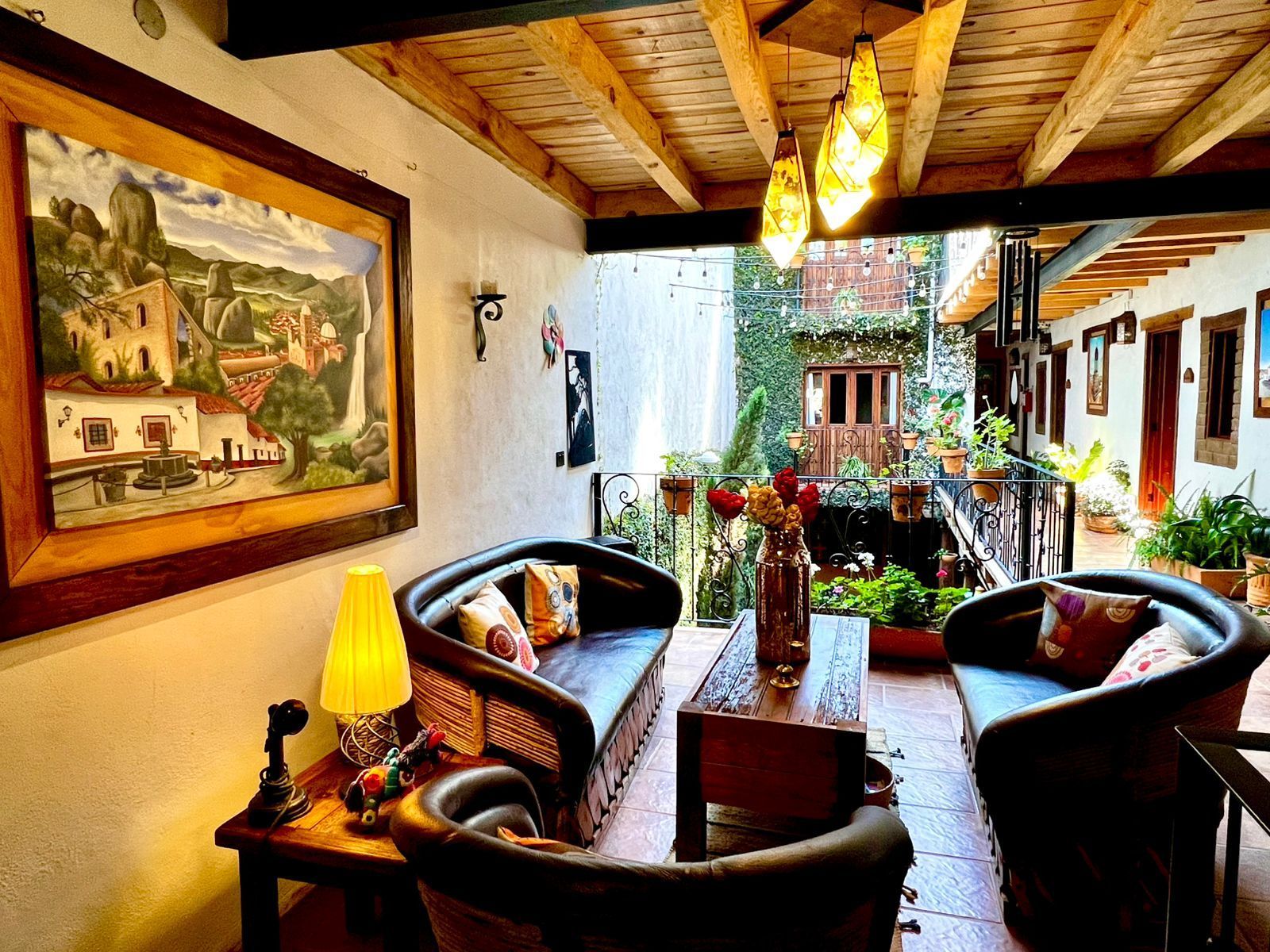 Una acogedora zona de estar exterior cubierta, con techos rústicos de madera, sofás de cuero oscuro y un cuadro en la pared.