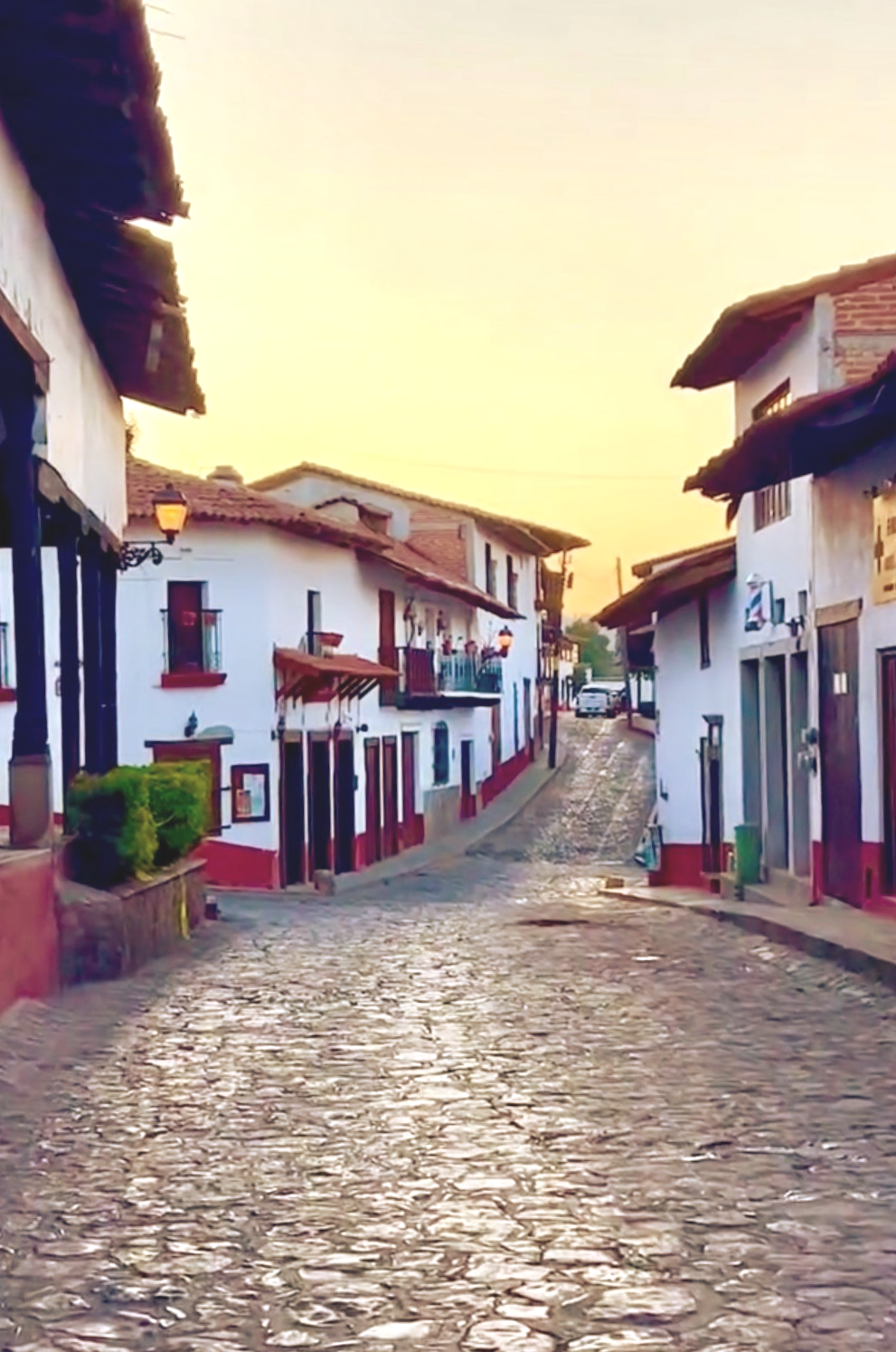 Una calle empedrada serpentea entre edificios blancos de estilo colonial en Tapalpa Pueblo mágico 